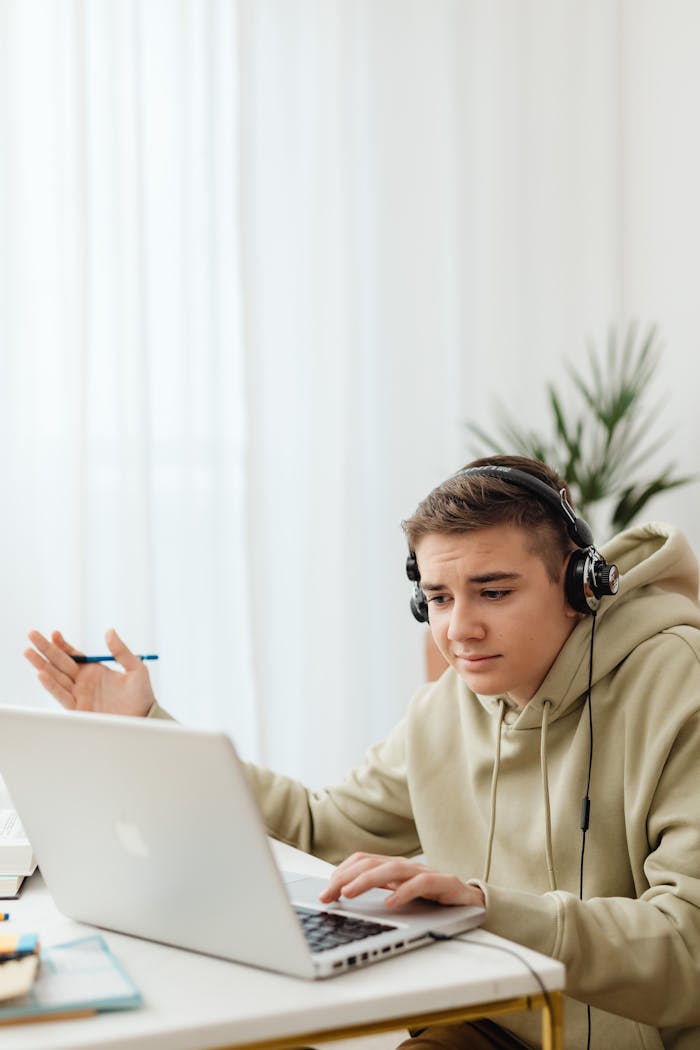 Teenager in hoodie using laptop for online learning at home.